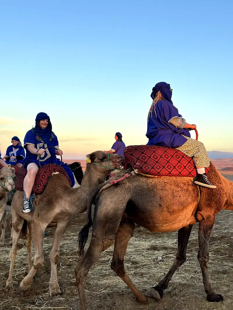 Traveller in traditional dress riding a camel at sunset in Agafay